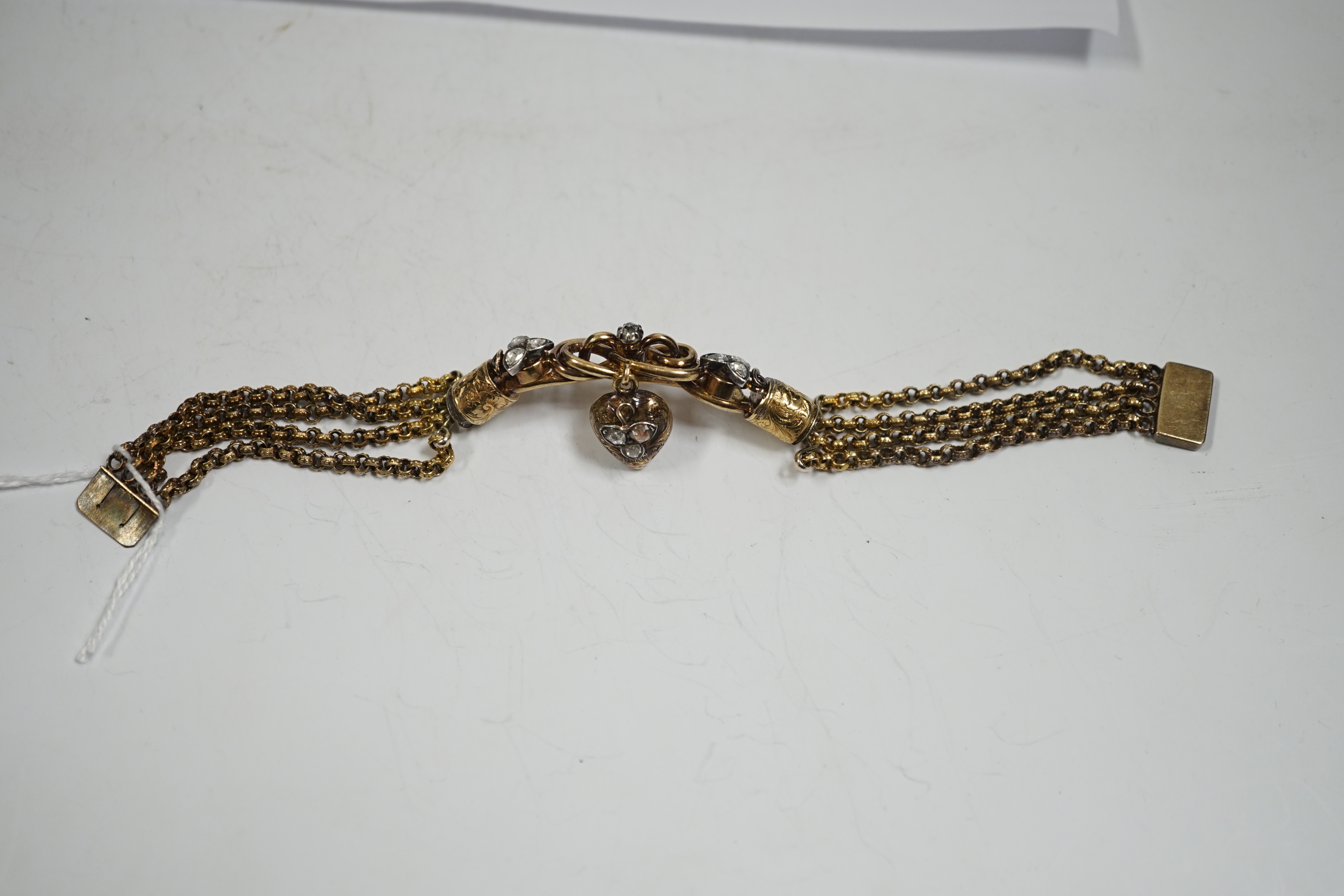 An antique yellow metal (test as 18ct) and rose cut diamond set triple strand bracelet, the central scrolling motif, hung with diamond set heart shaped charm, approx. 17cm, gross weight 30 grams.